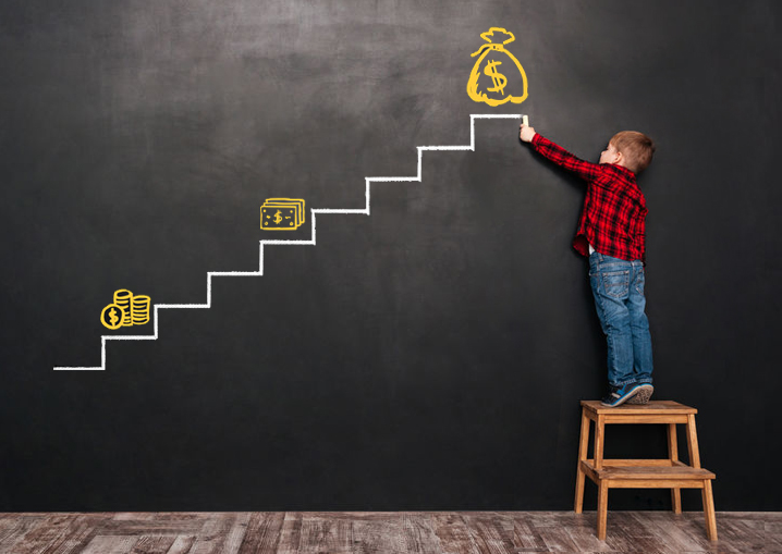 Photo of a little cute child standing on stool near blackboard and drawing on it.
